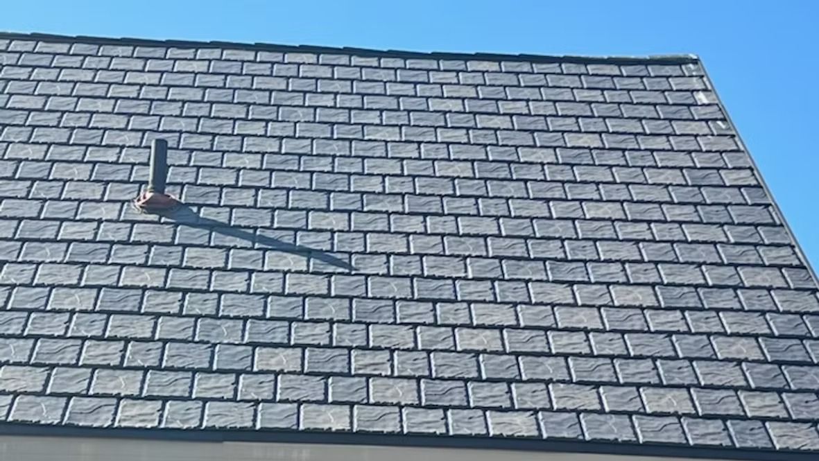 Gray shingled roof with a vent pipe casting a long shadow under a clear blue sky