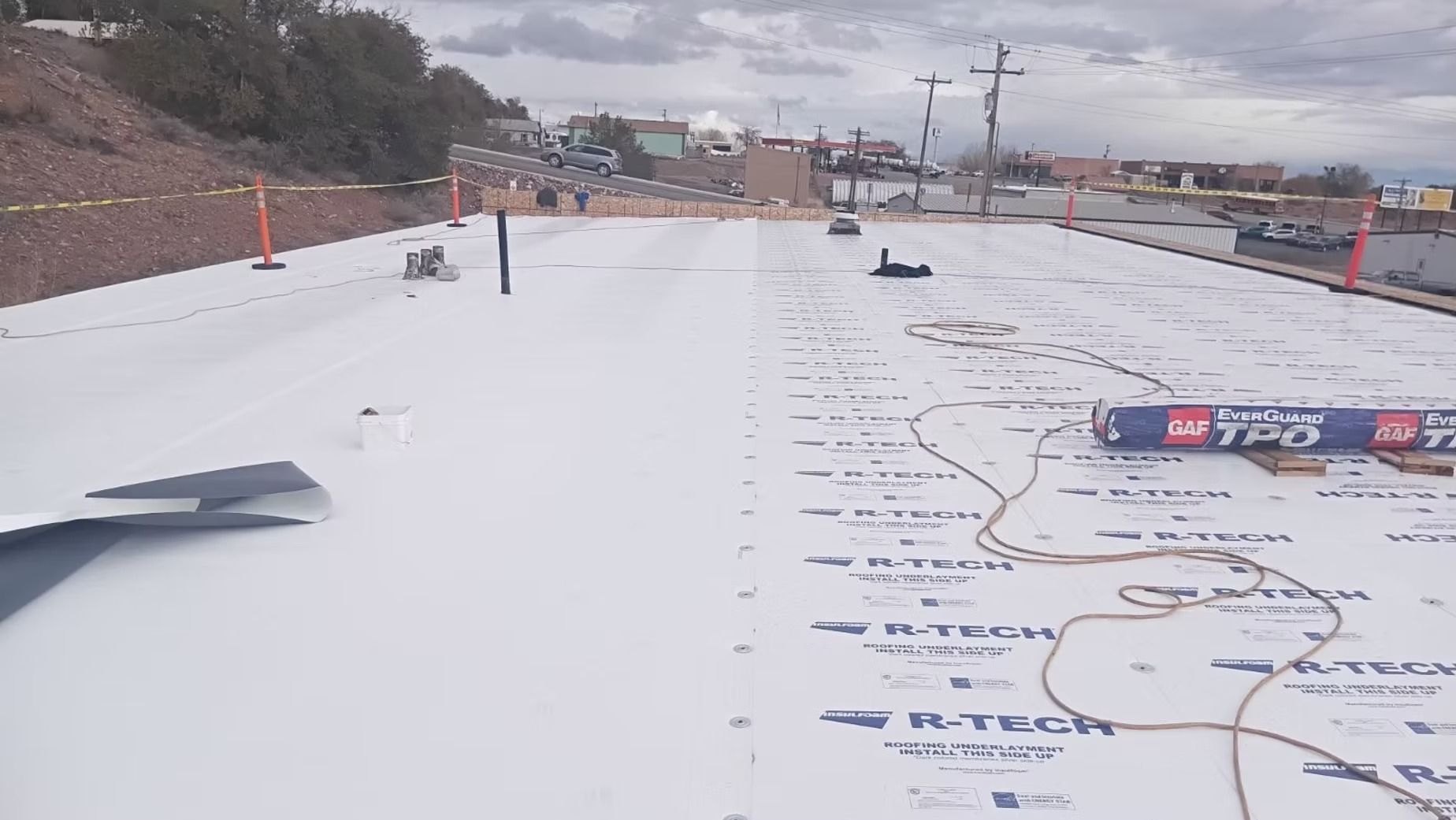 Flat commercial roof with white membrane; construction materials and tools visible.
