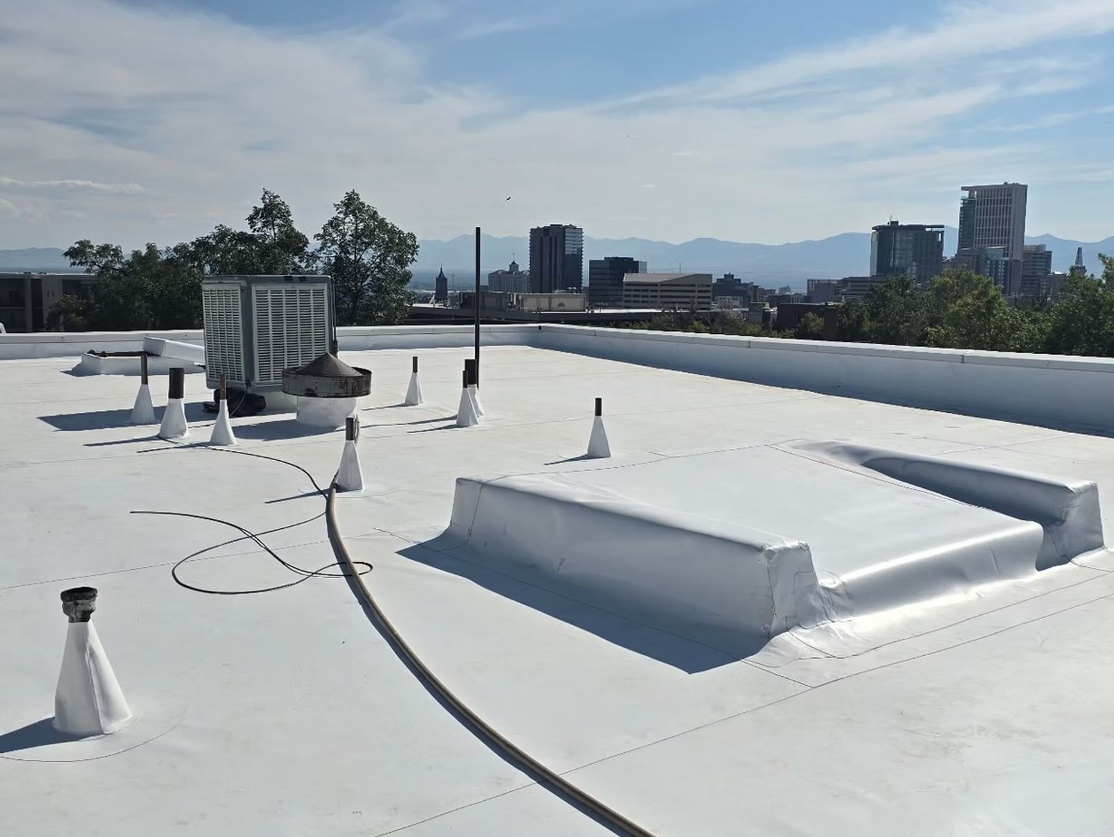 Flat white rooftop with cityscape background; equipment and pipes visible.