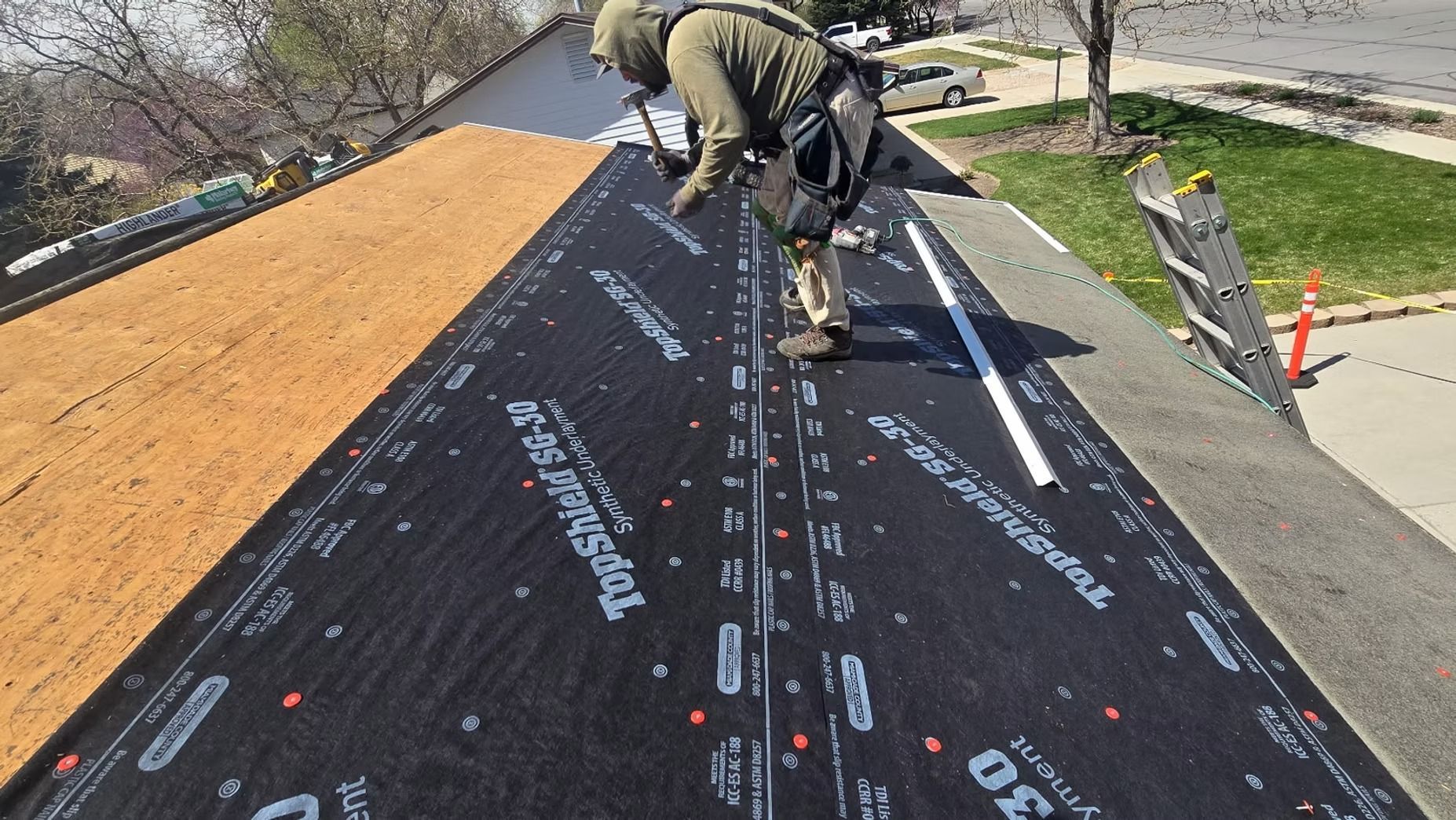 Roofer on a sloped roof installing black roofing underlayment.