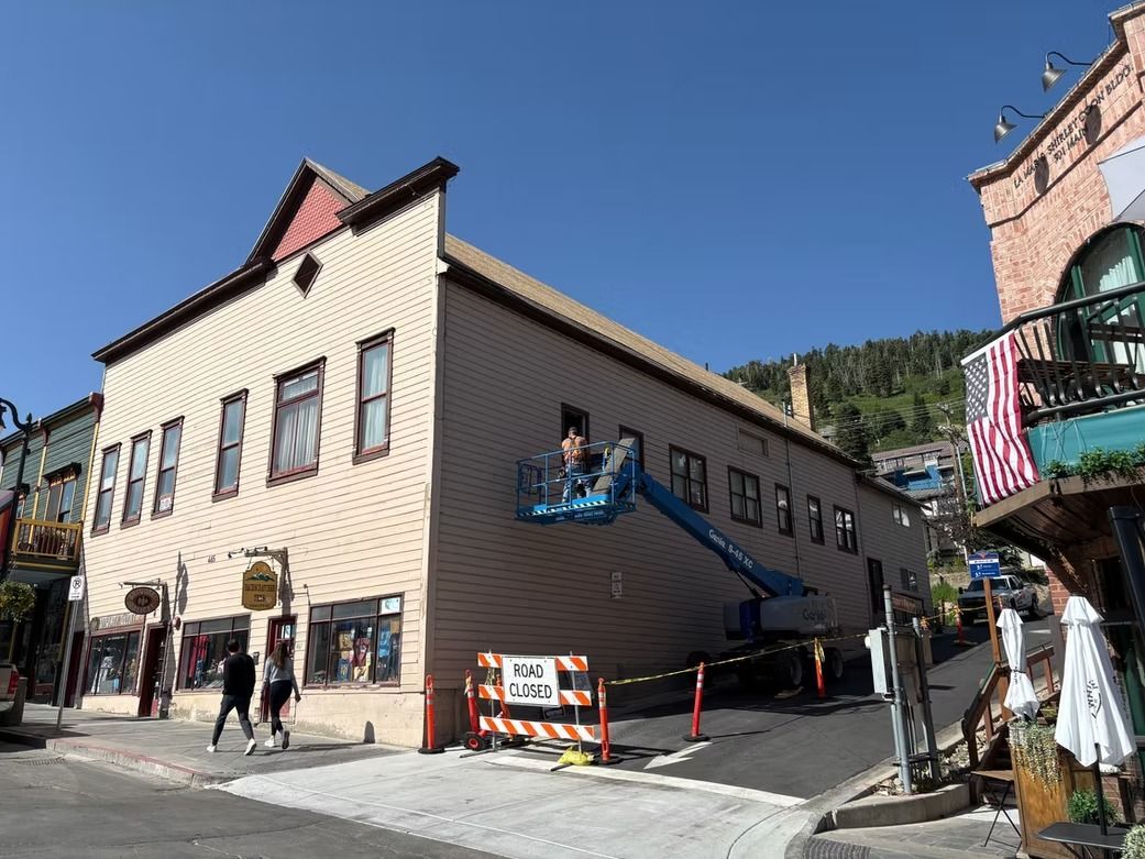Two-story beige building on a street, with construction in progress. A lift is near the window.
