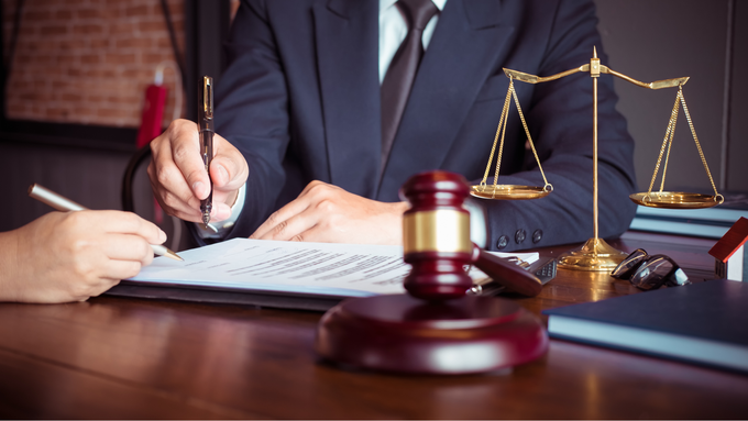 A man in a suit and tie is sitting at a table with a judge 's gavel and scales of justice.