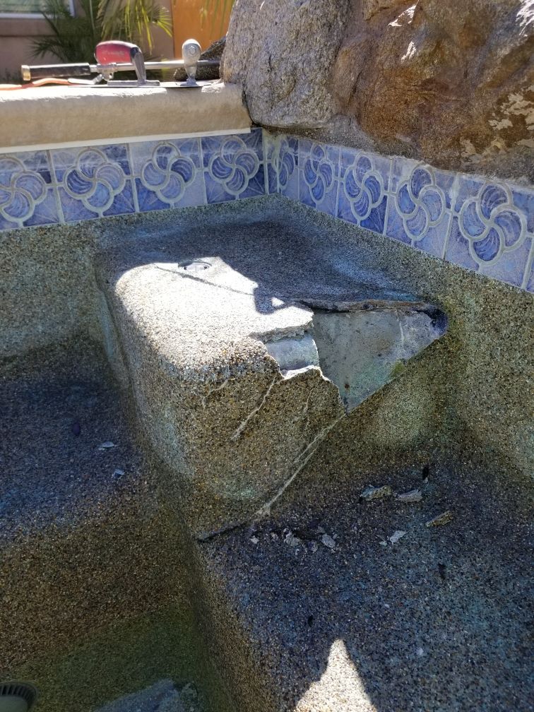 A swimming pool with a broken tile border and a rock in the middle.