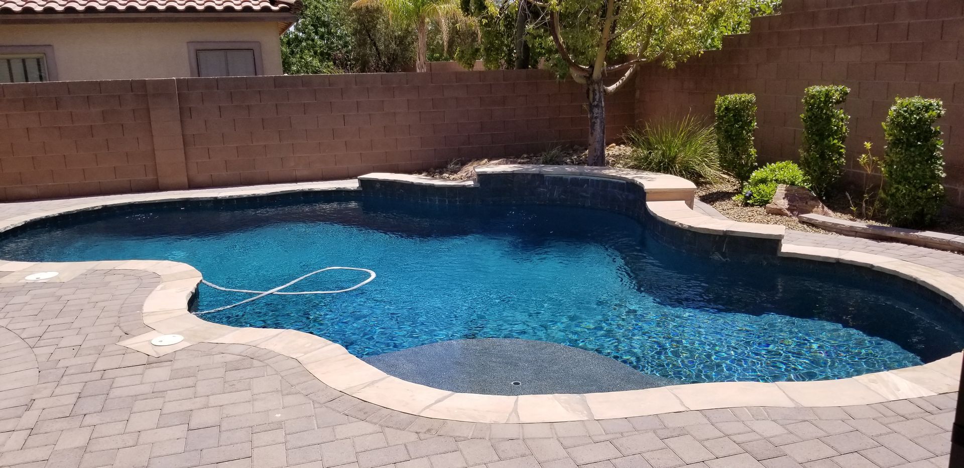 A large swimming pool with a brick patio in front of a house.