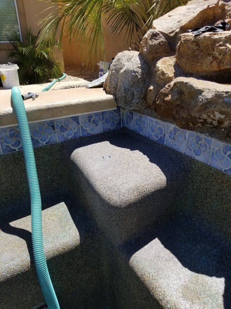 A green hose is attached to the side of a swimming pool.