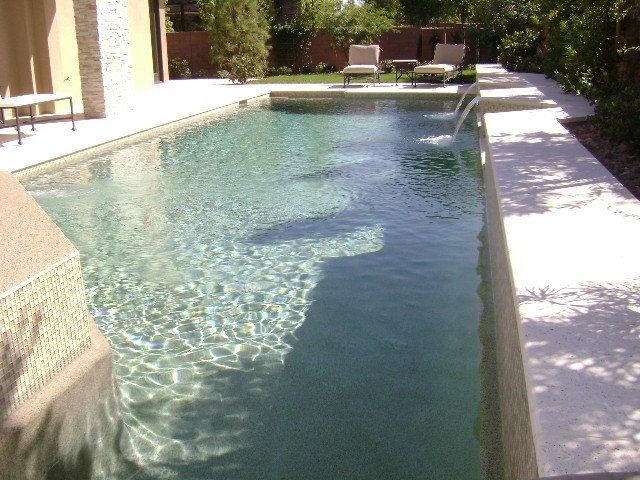 A large swimming pool is surrounded by chairs and trees