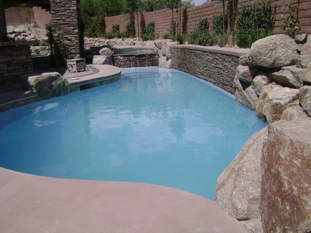 A large swimming pool surrounded by rocks and a stone wall.