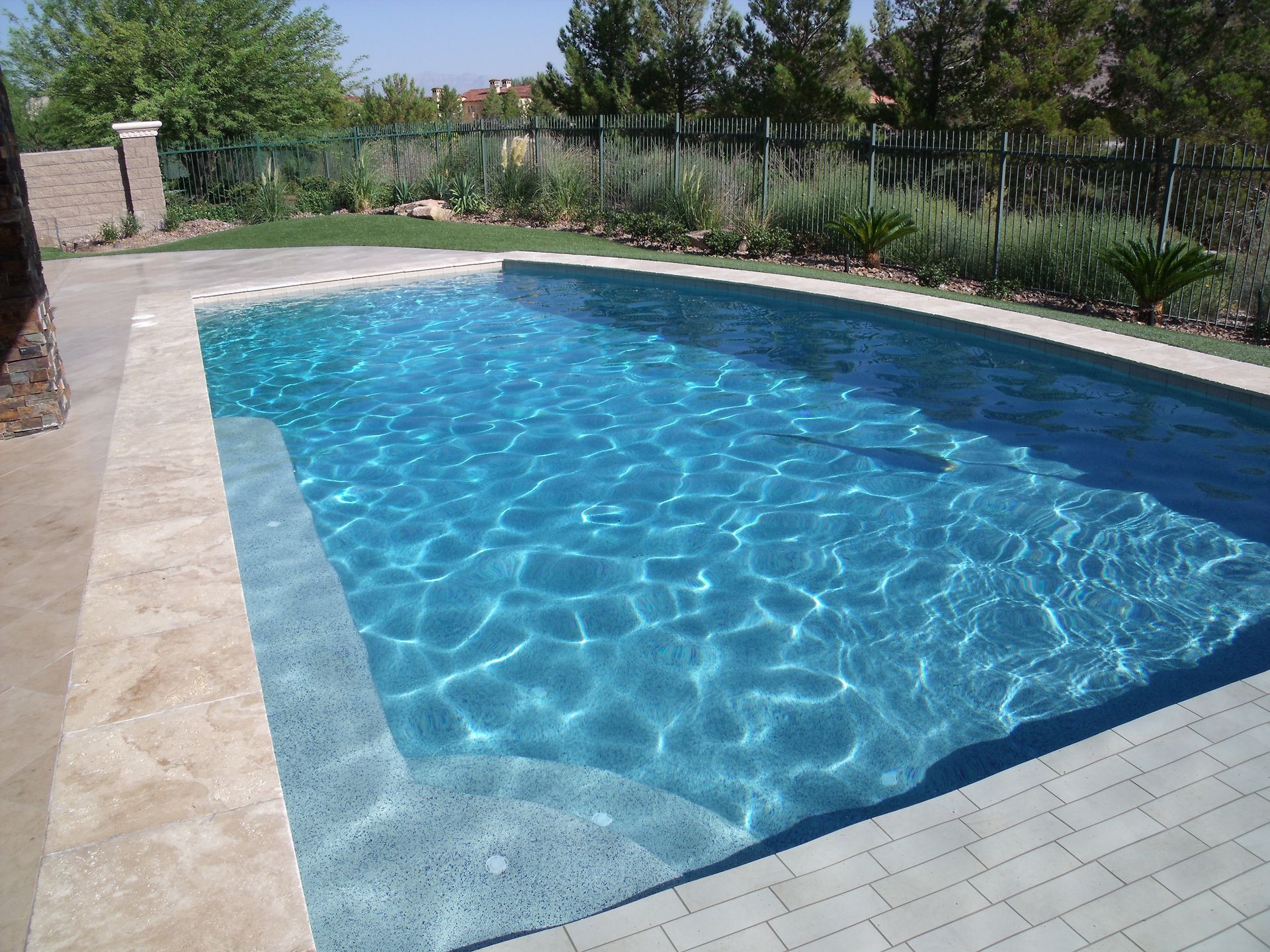 A large swimming pool is surrounded by bricks and trees