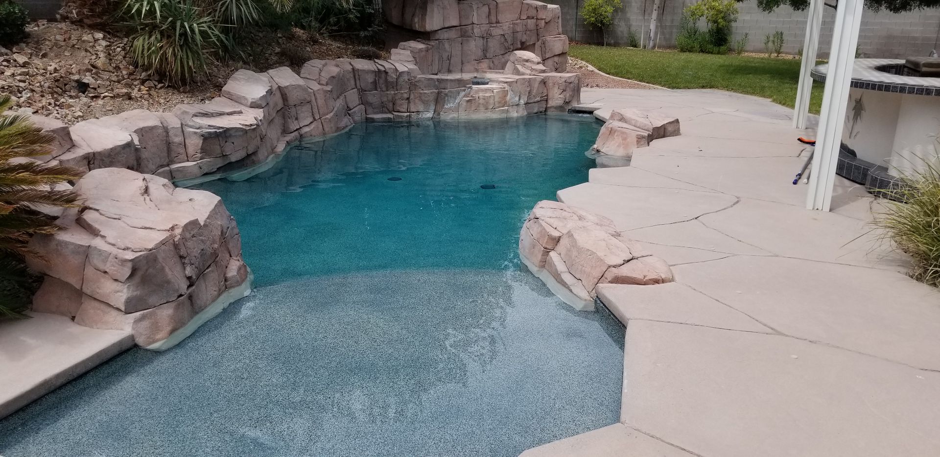 A large swimming pool surrounded by rocks in a backyard.