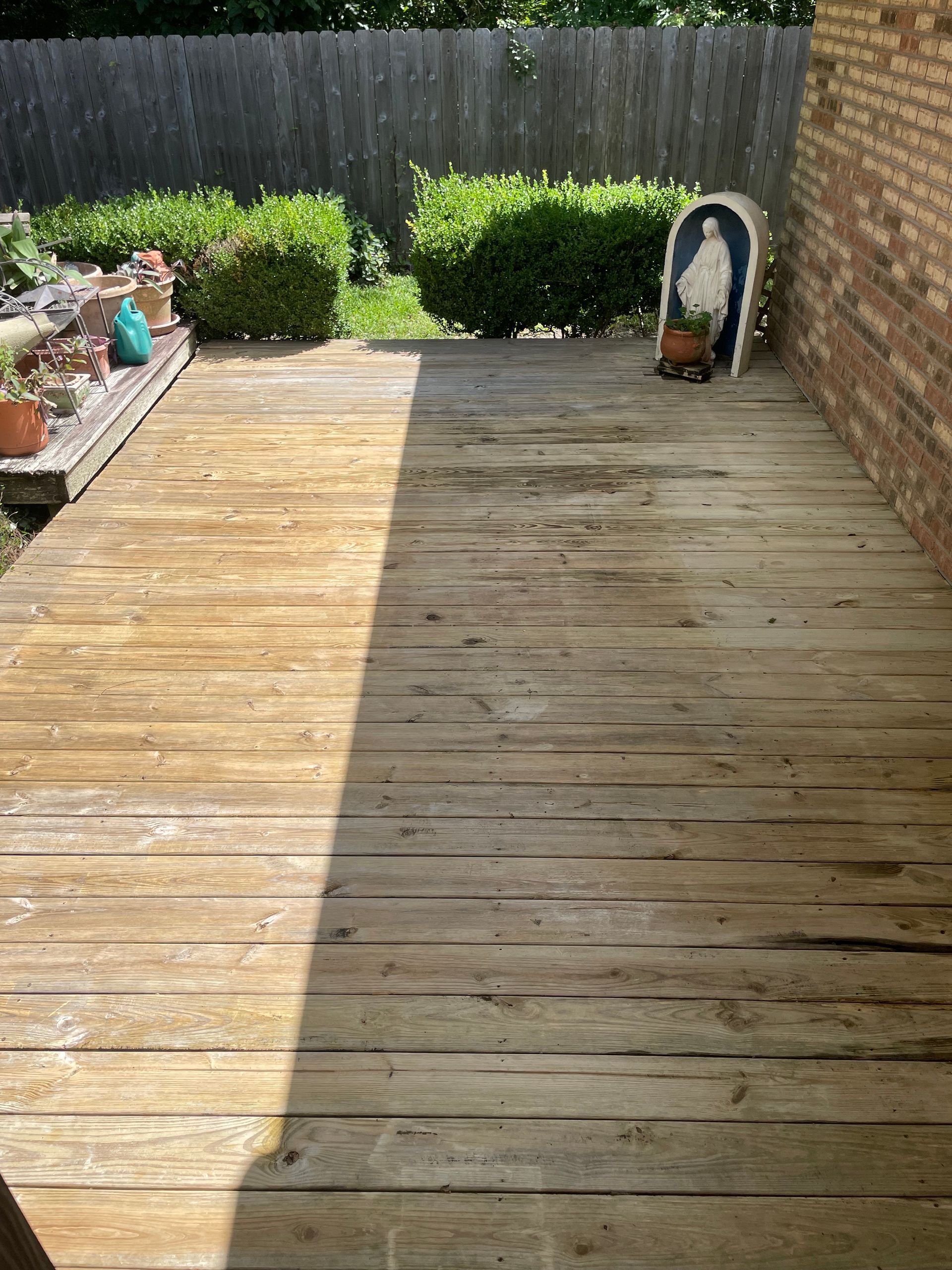 Wooden deck with faded color, next to brick wall and garden.