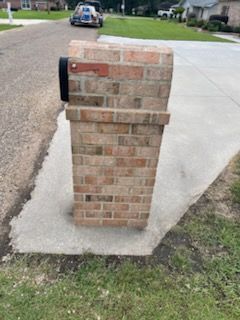 Brick mailbox on a concrete pad next to a street. Black mailbox attached.