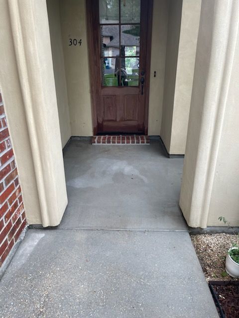 Entrance with concrete floor, brick wall left, beige pillars, wooden door with glass, and a doormat.