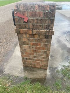 Brick mailbox with a red flag, set on a concrete pad, wet from cleaning.