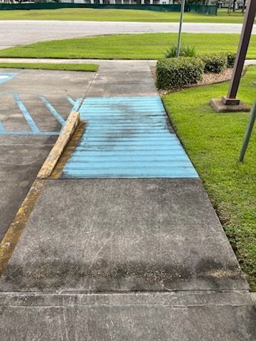 Blue ramp on a sidewalk next to a grassy area and parking space.