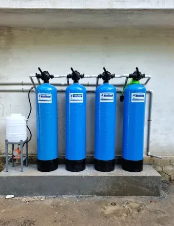 Four blue water filtration tanks installed on a concrete platform against a white wall with a small white storage tank.
