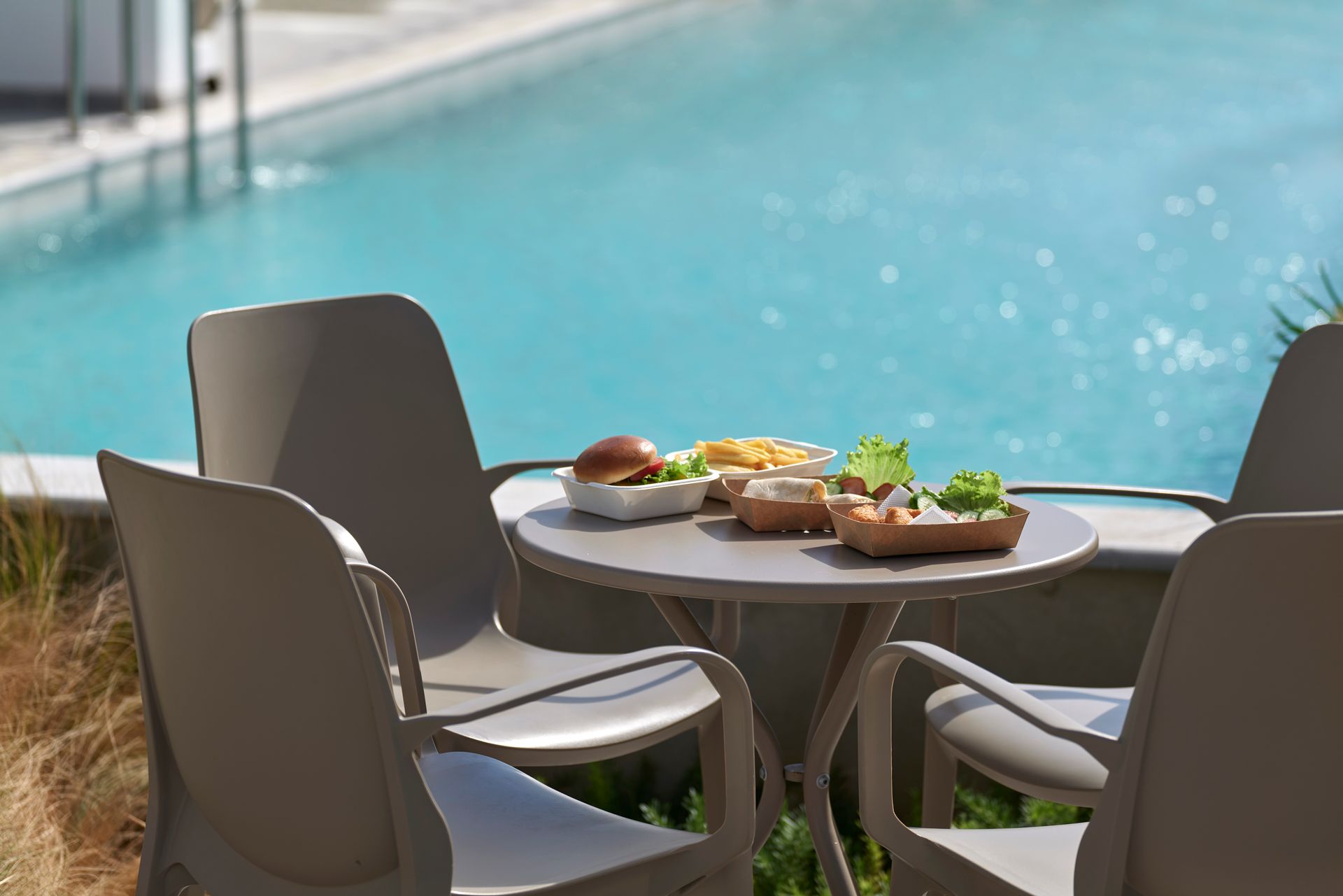 Table set with food and chairs by a pool.