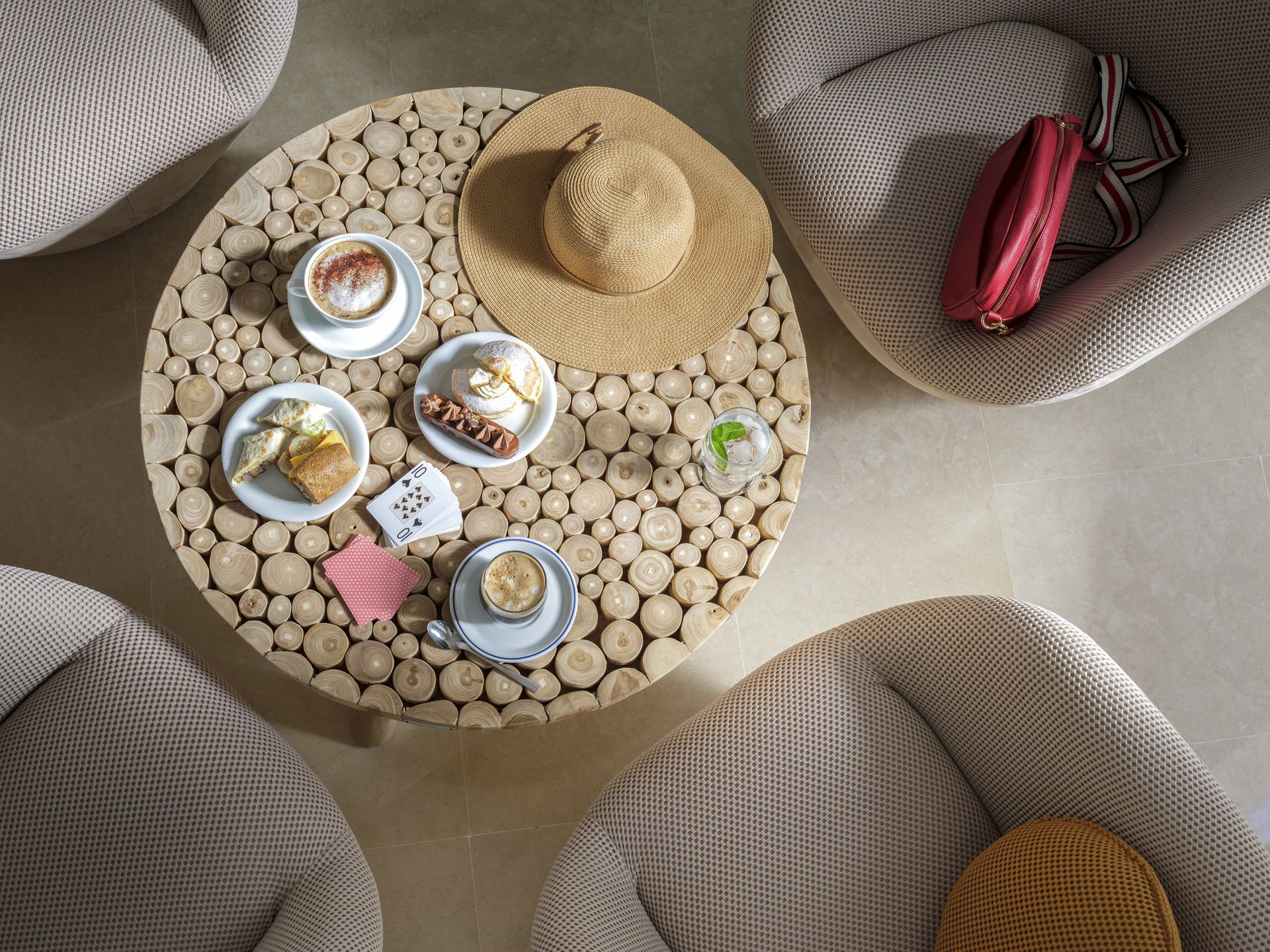 A bird's-eye view of a coffee table with food and drinks, surrounded by woven chairs, and a sun hat.