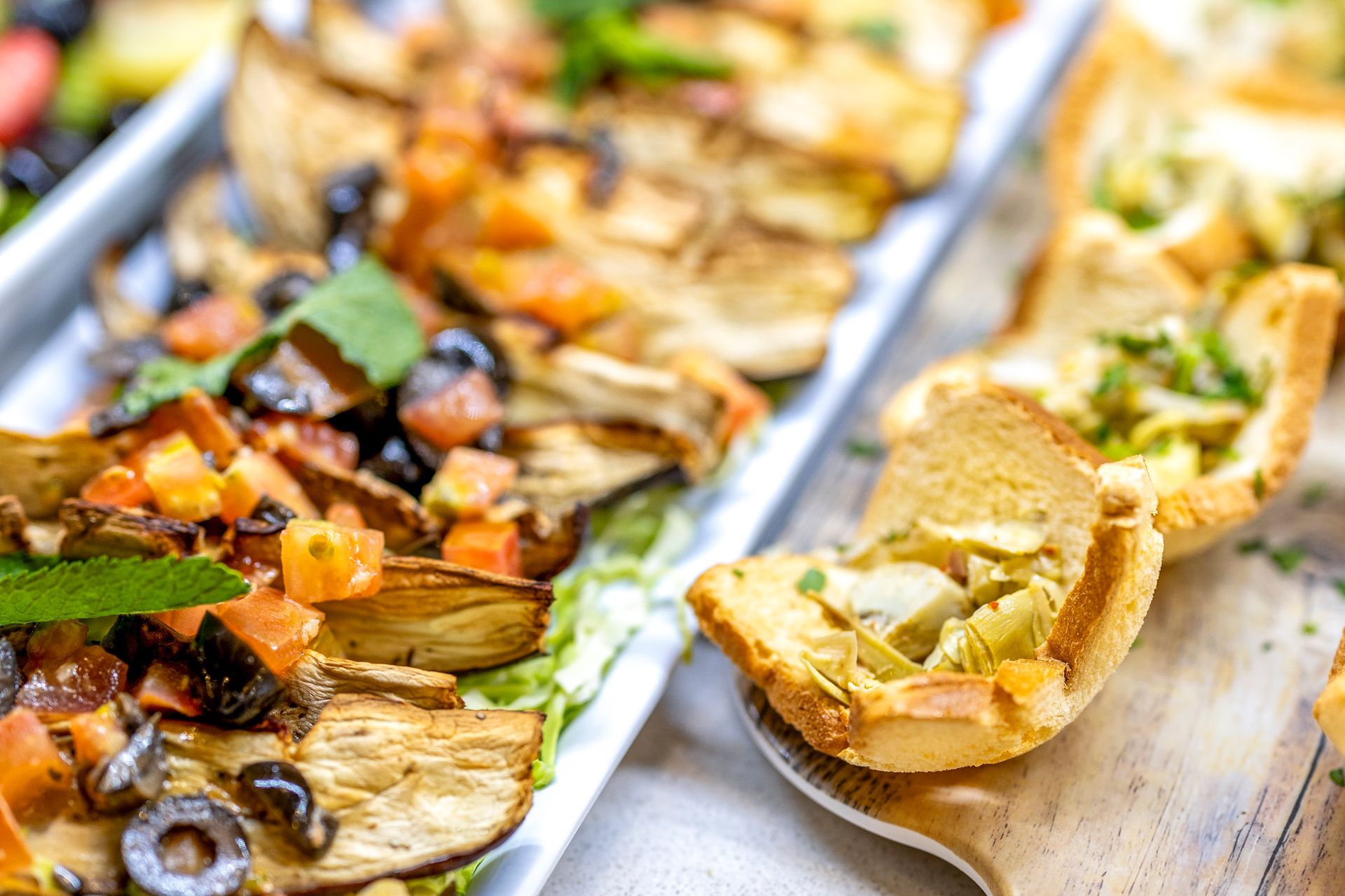 Appetizer platter with toasted bread topped with vegetables, olives, and herbs.