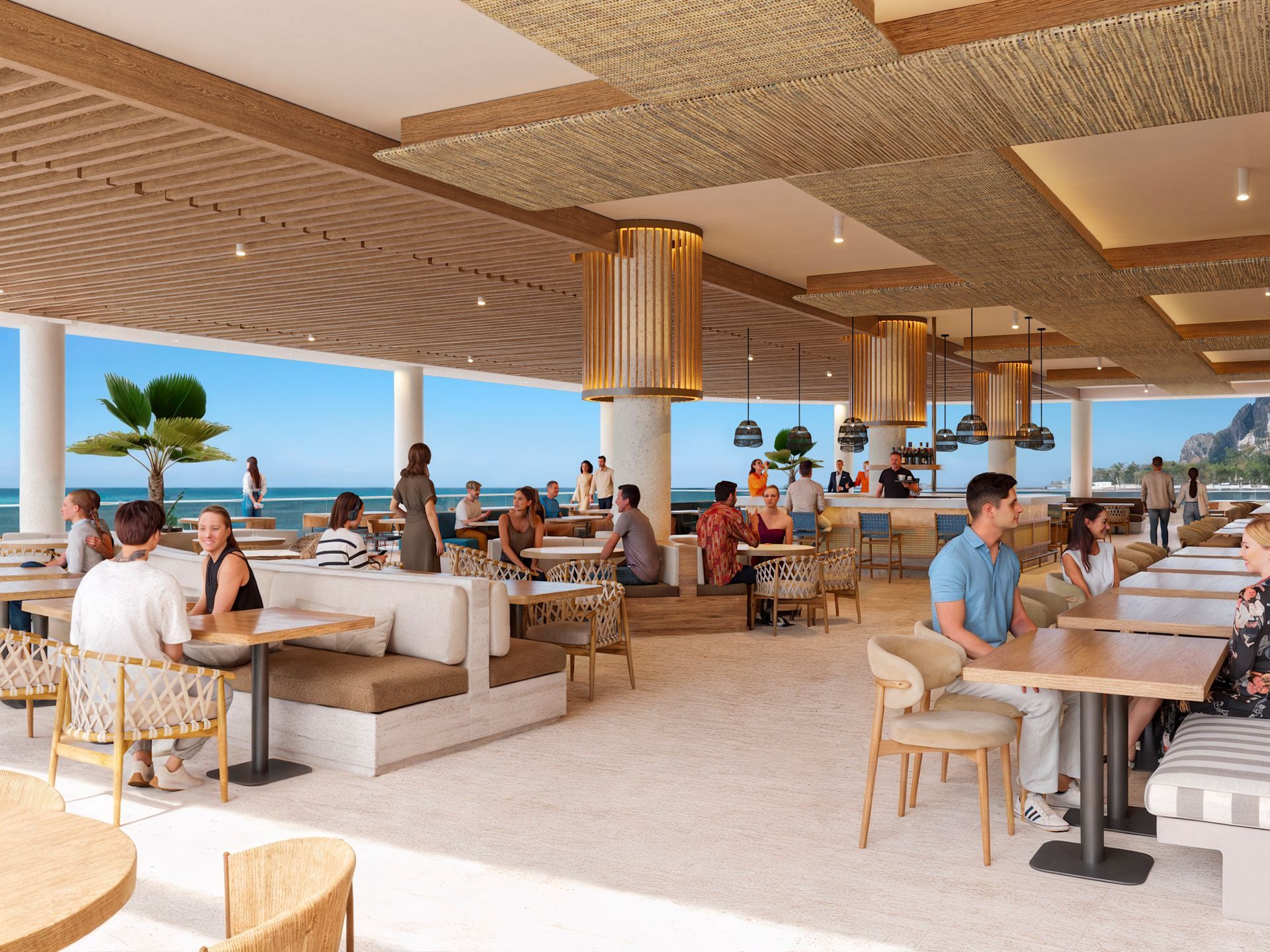 Mensen dineren in een restaurant aan het strand met uitzicht op de oceaan, licht houten en rotan meubilair, in de openlucht.