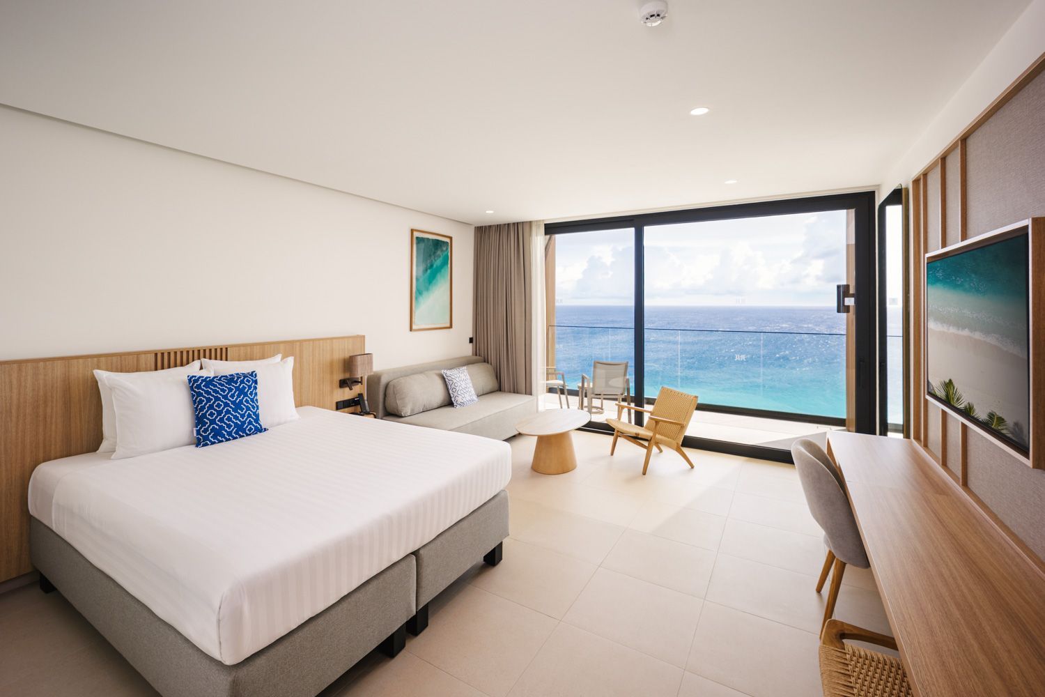 Cozy hotel bedroom with a bed, sofa, and wood accents. Neutral tones, including light wood and white bedding.