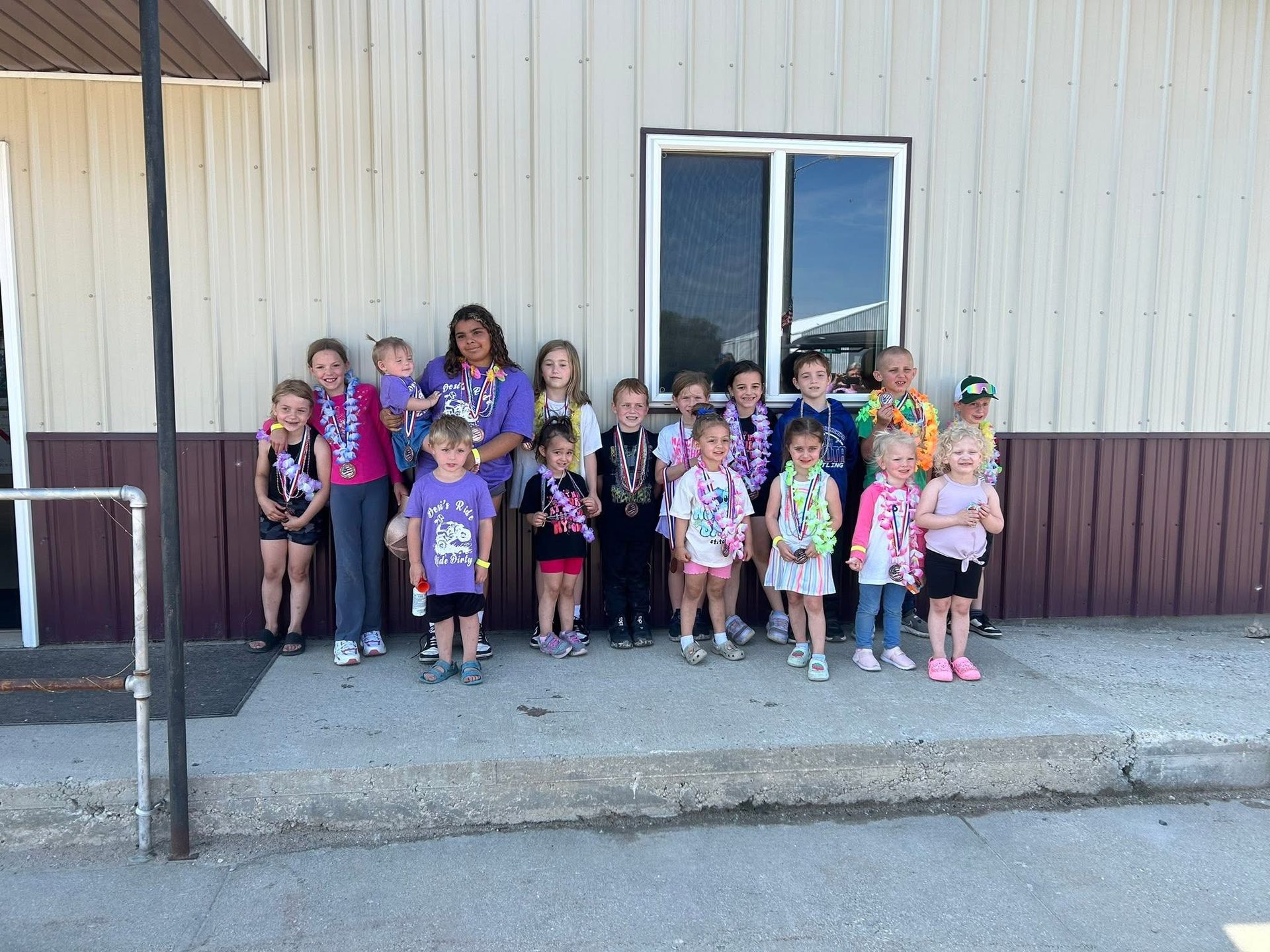 Group of children posing outside a beige building near a doorway and window