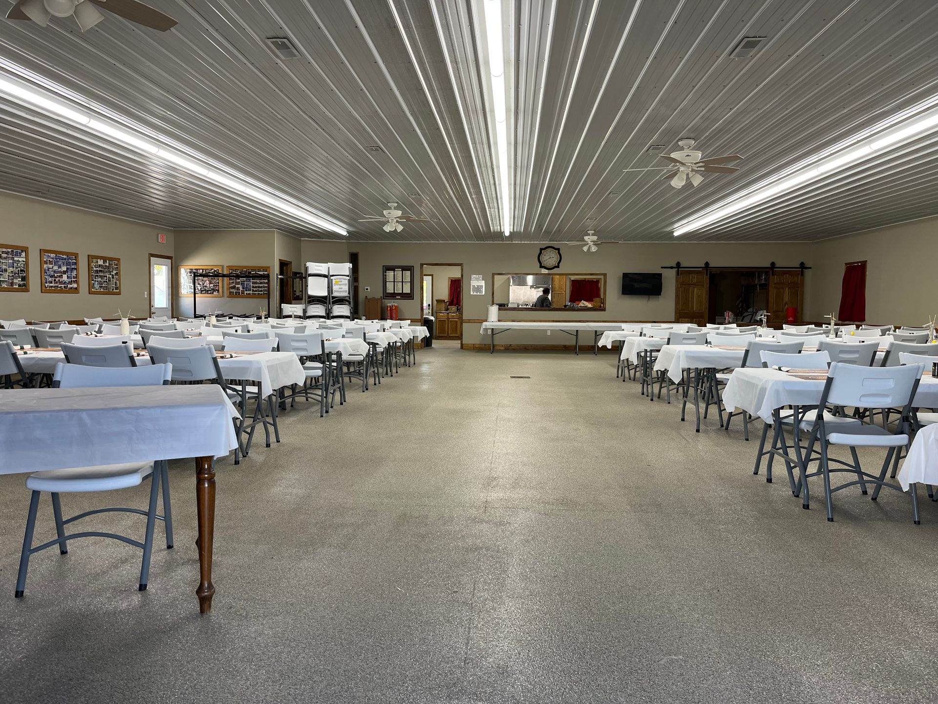 Large banquet hall with rows of white-covered tables and chairs under bright fluorescent lights