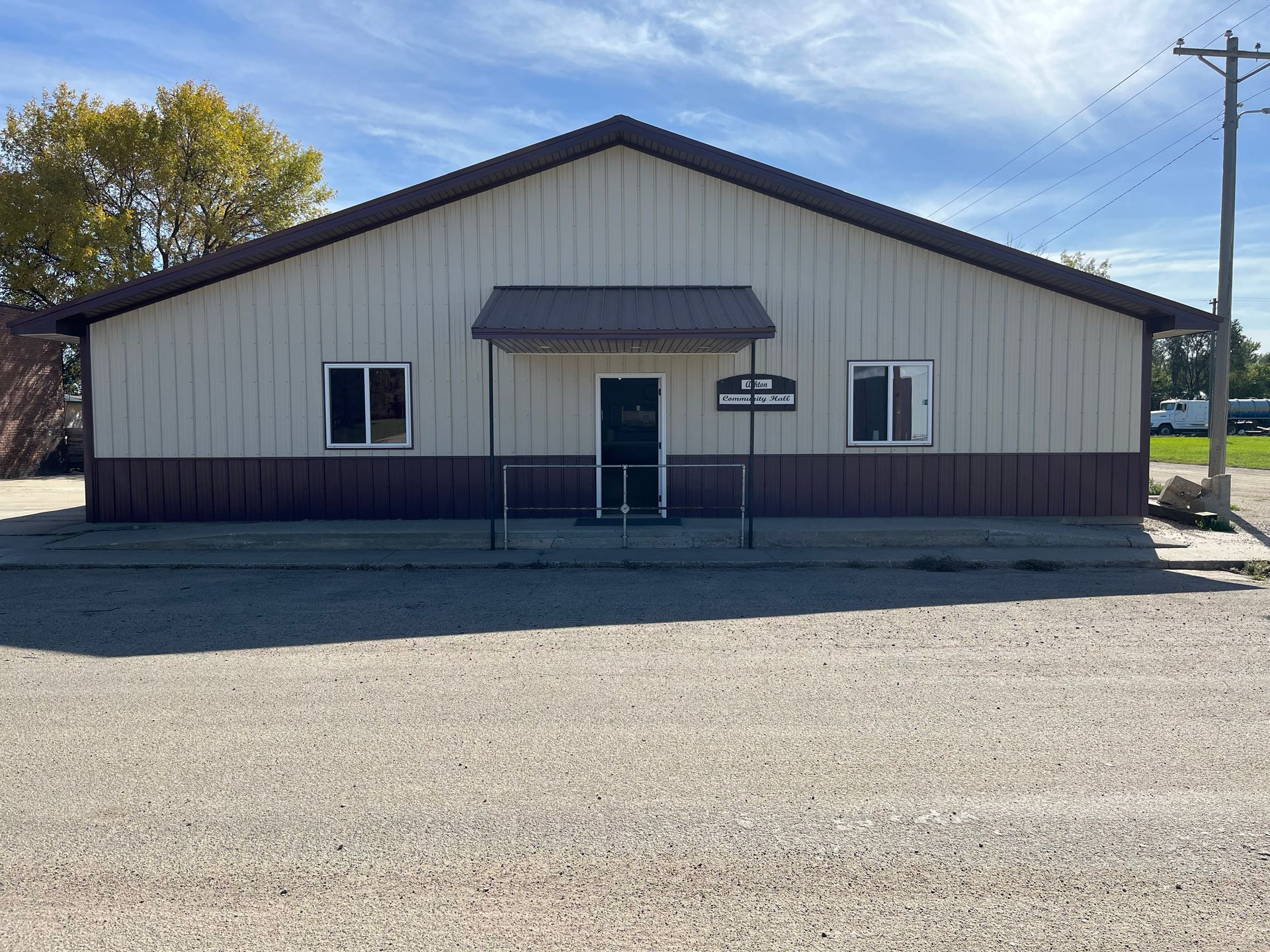 Front view of a small white building with a dark roof and gravel foreground on a clear day