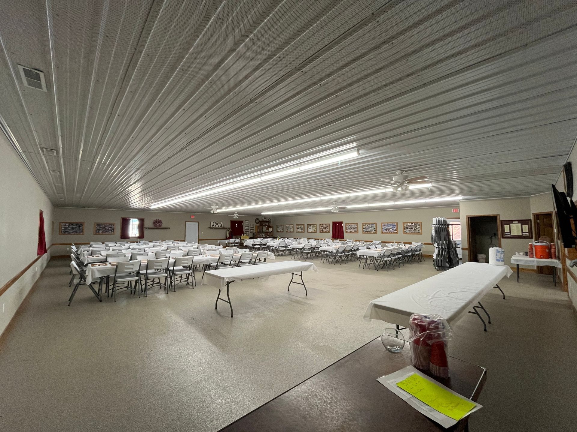 Large banquet hall with rows of white-covered chairs and tables under bright ceiling lights