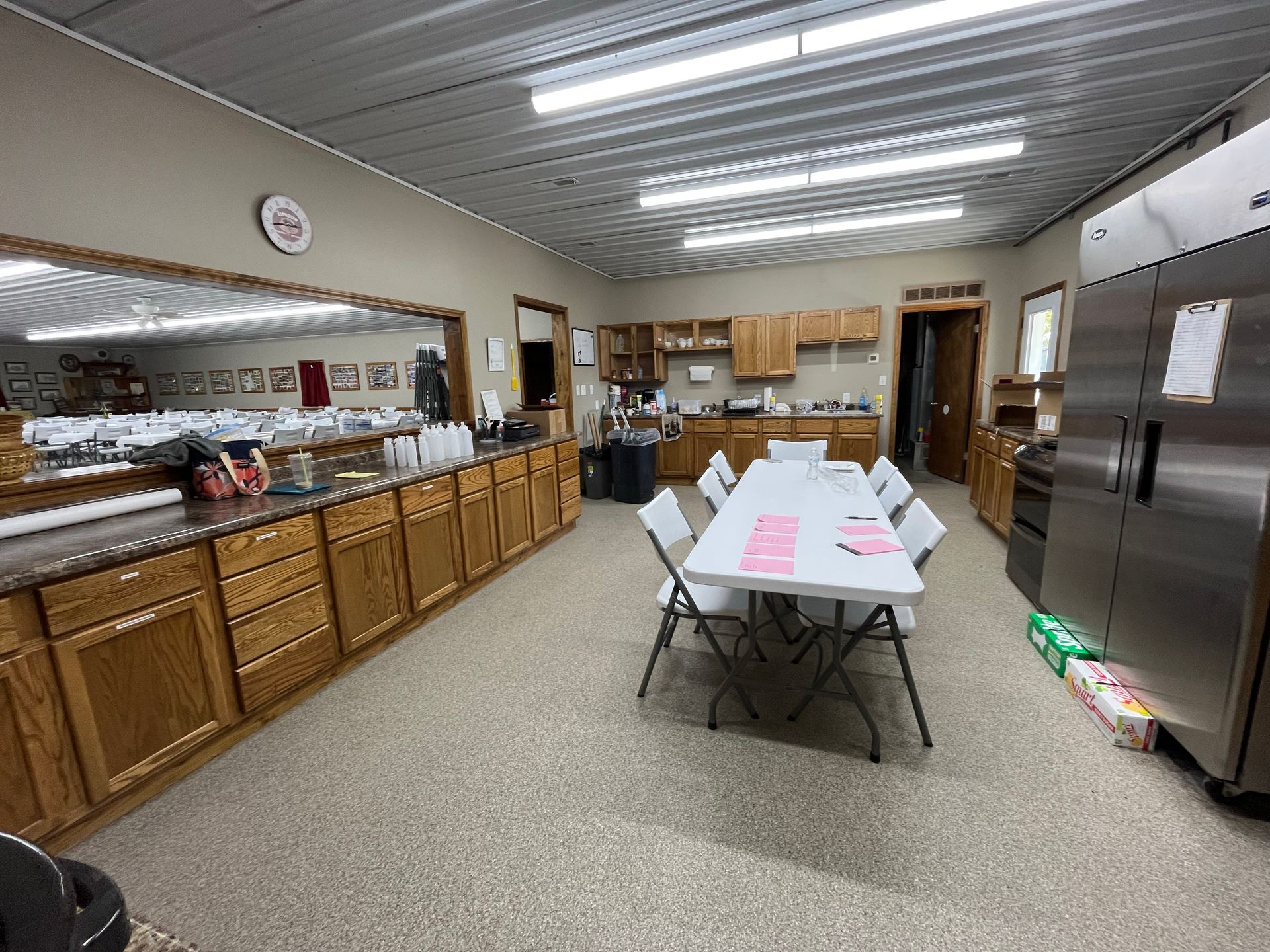 Community kitchen with tables, cabinets, stainless steel appliances, and fluorescent ceiling lights