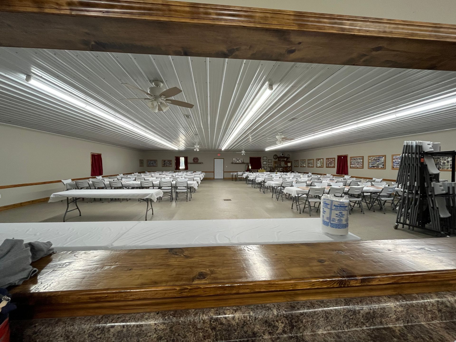 Empty banquet hall with long rows of tables and white chairs under bright ceiling lights