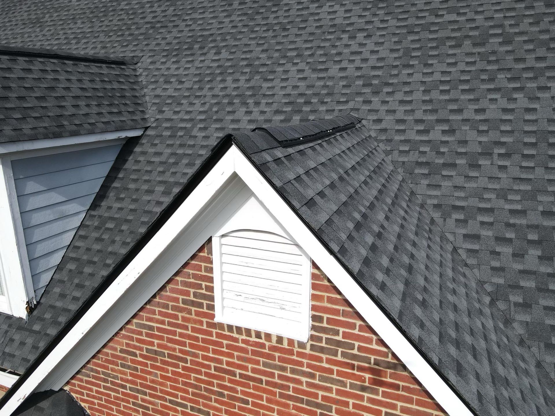 Roof with gray shingles, white trim, and a red brick gable vent.
