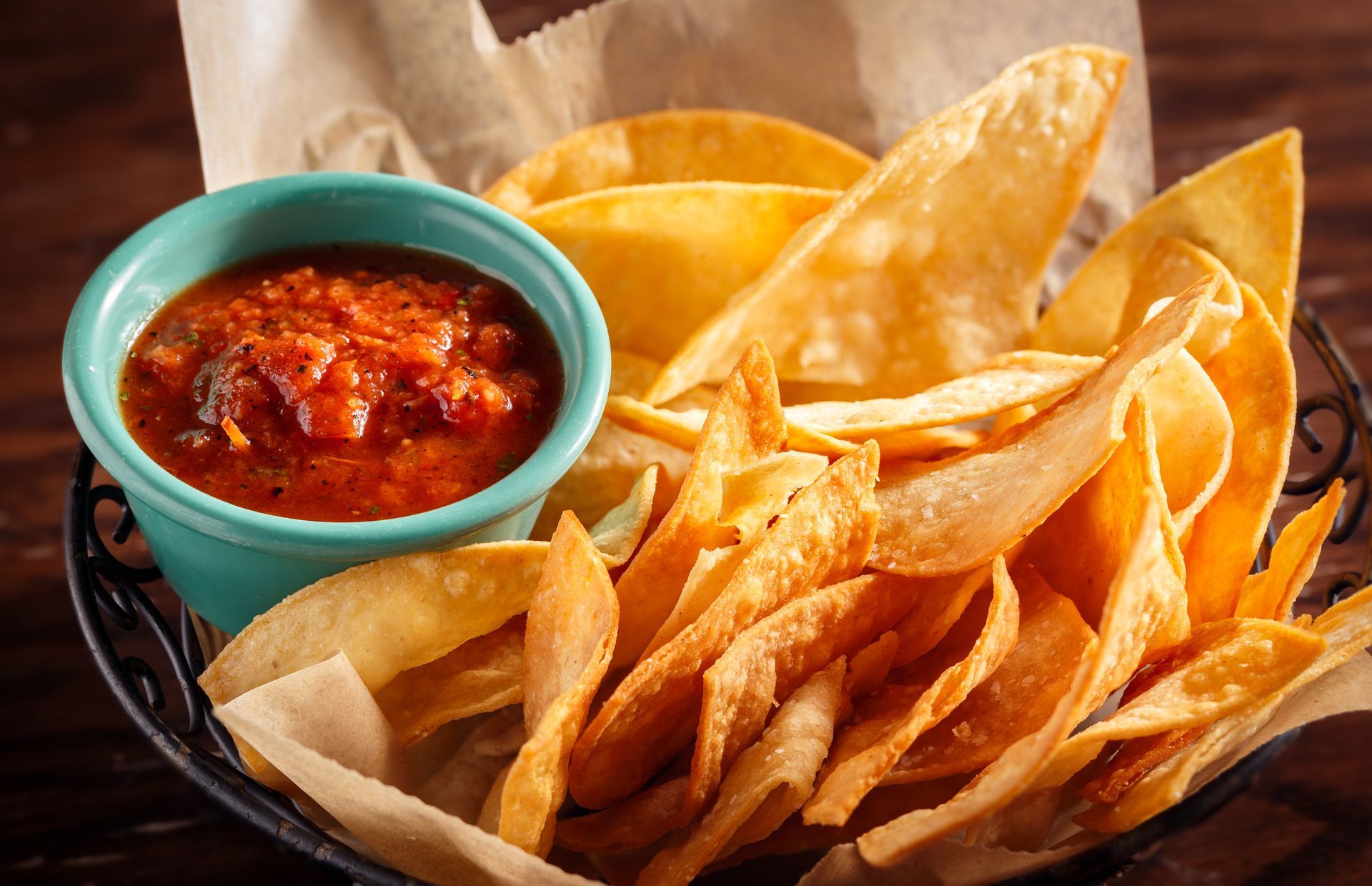 Basket of tortilla chips with salsa in a teal bowl