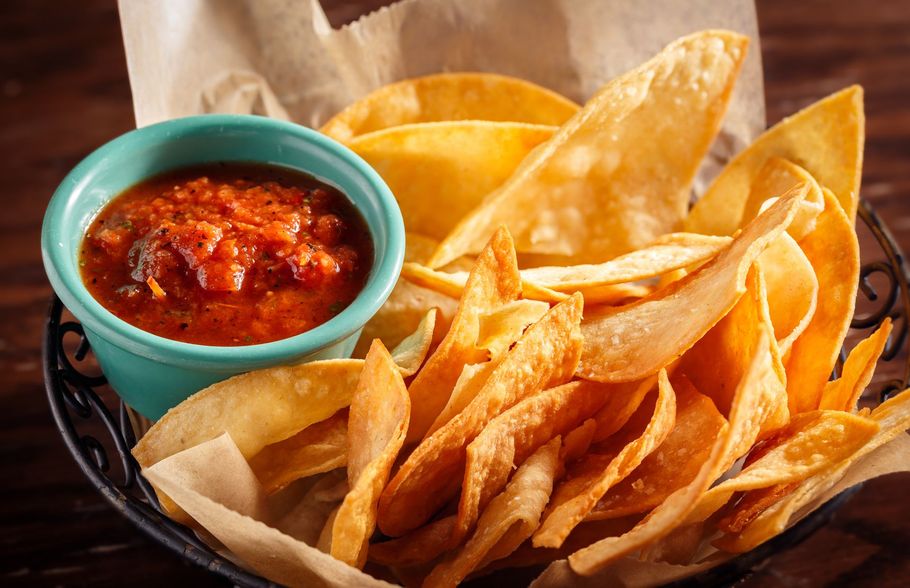 Tortilla chips in a black basket with a teal bowl of red salsa