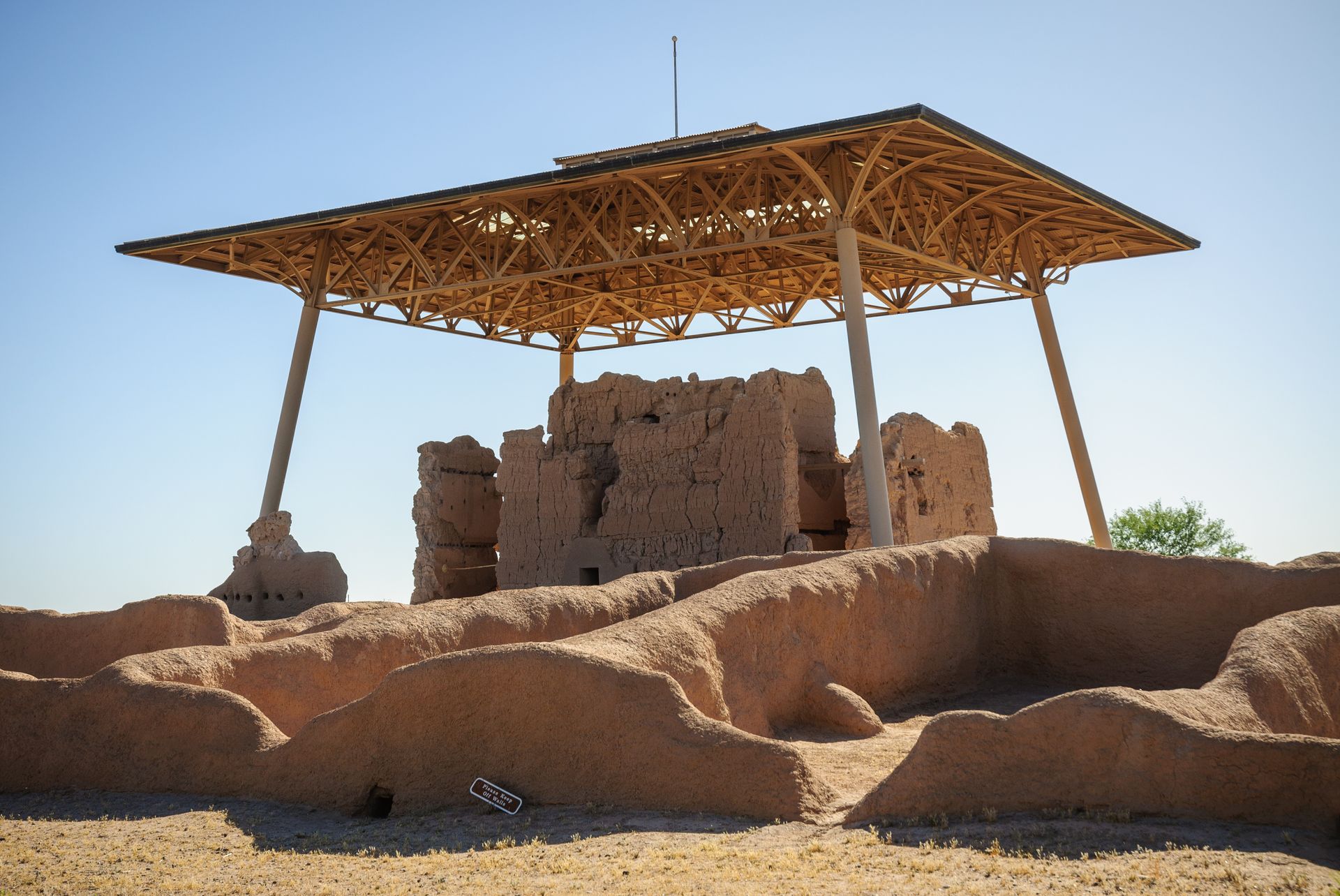 Ruins under a metal canopy in a dry, sandy landscape under a clear sky