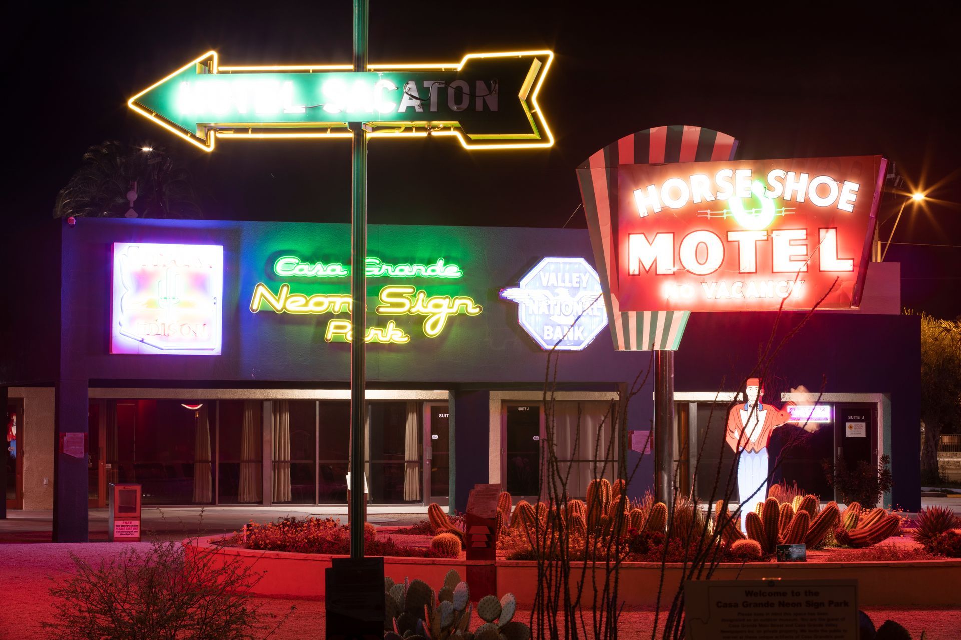 Neon-lit roadside motel at night with bright signs and a colorful retro storefront