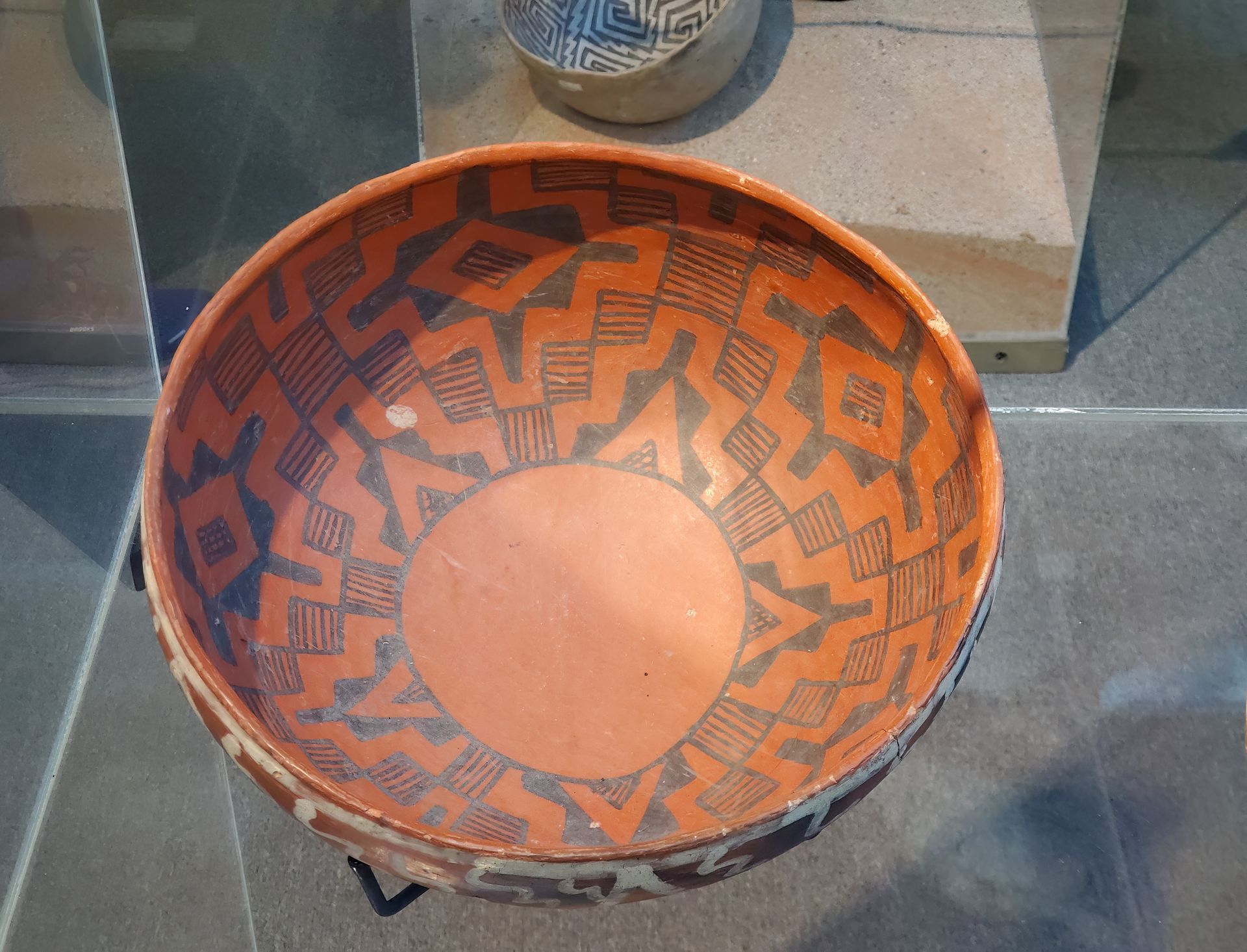 Orange and black patterned woven basket on a glass display surface