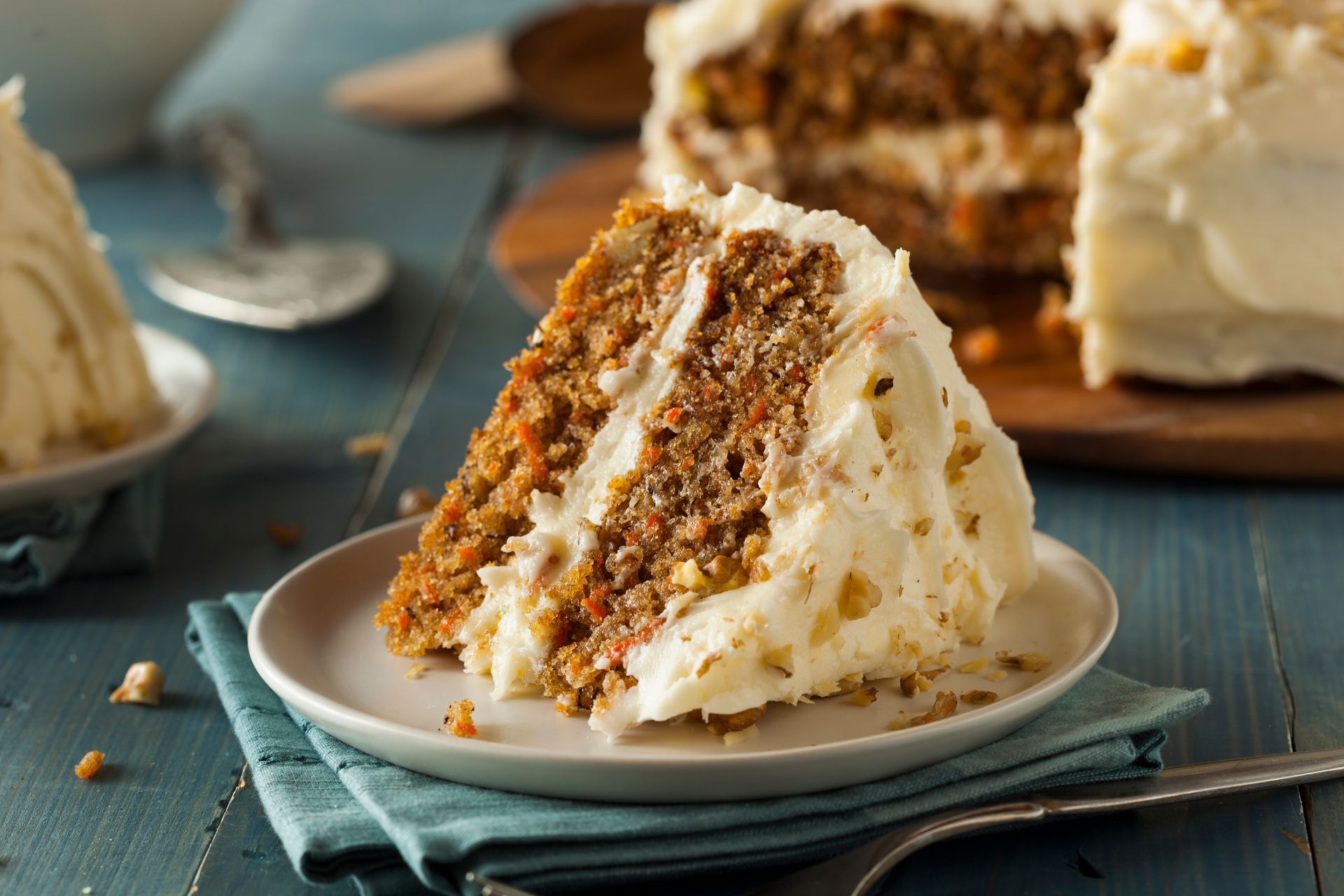 Slice of carrot cake with cream cheese frosting on a blue plate on a rustic table