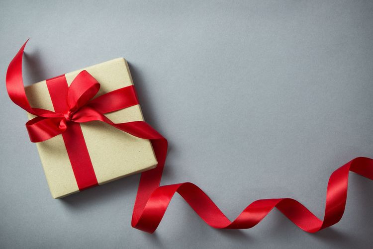 Gift box with a red ribbon and bow on a gray surface, ribbon trailing to the right