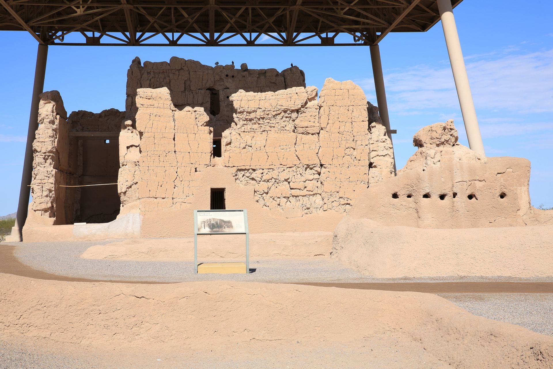 Ancient mud-brick ruins under a shade structure in a desert setting