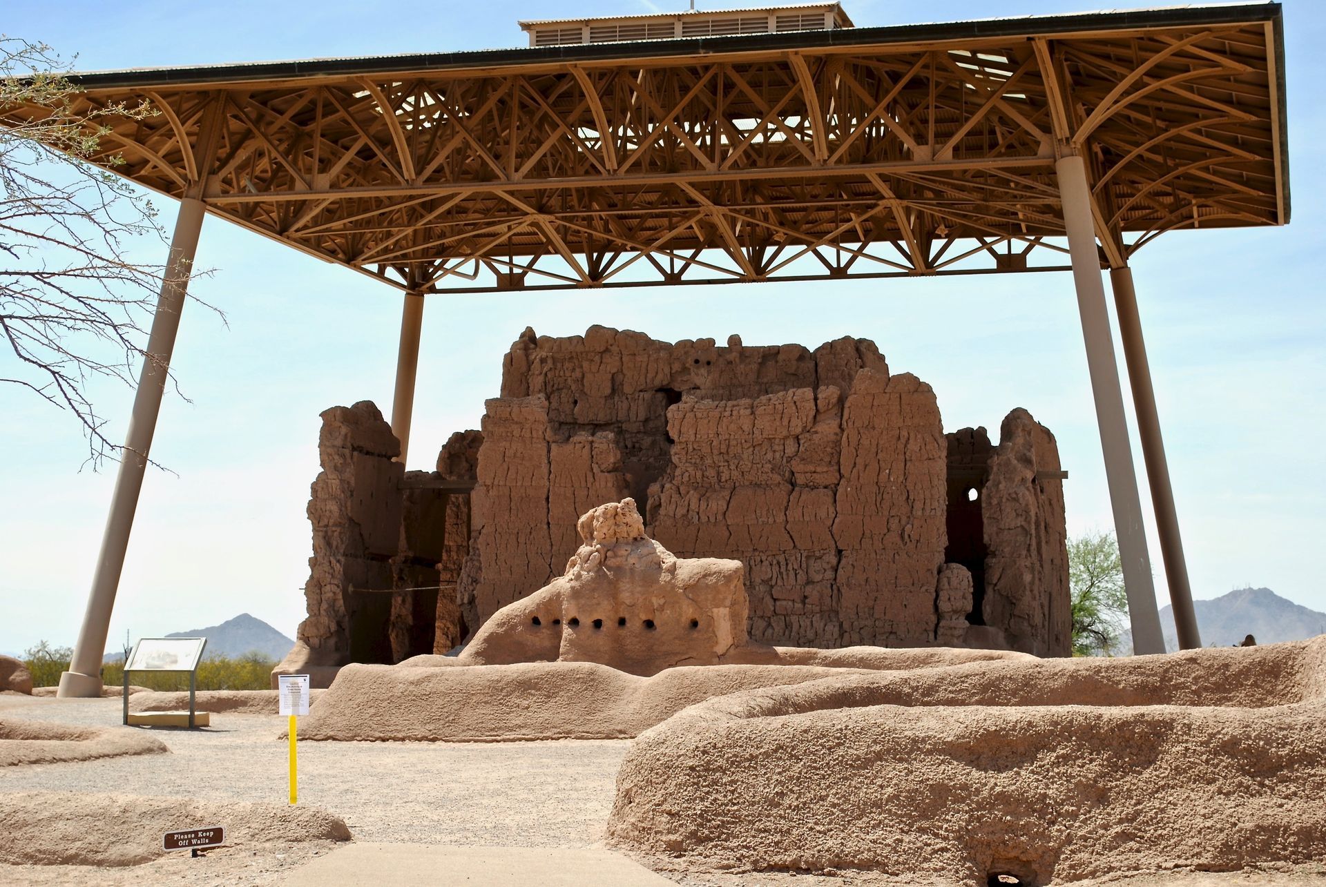 Ancient mud-brick ruins under a large protective canopy in a desert landscape