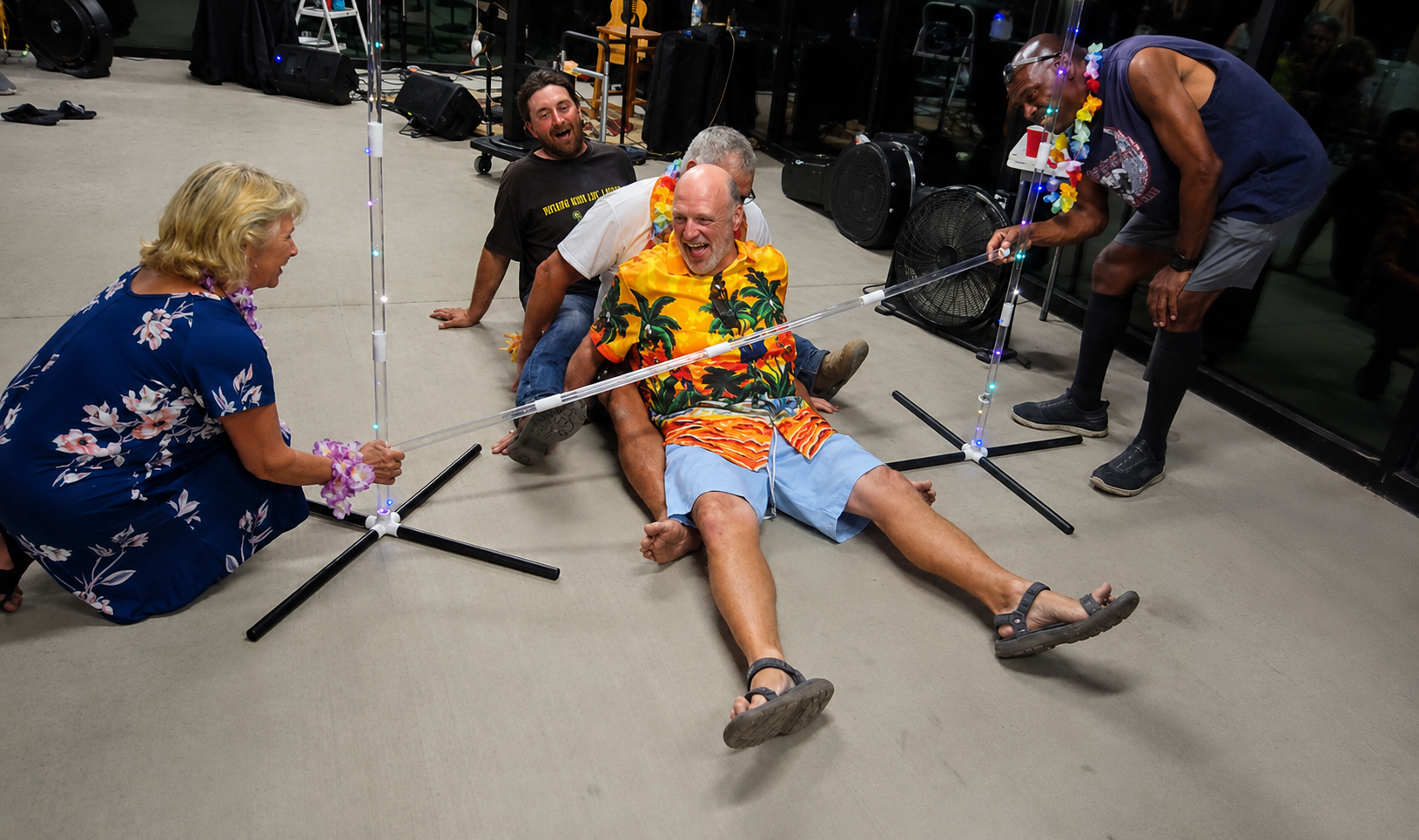 People seated on the floor during a group activity, using microphone stands as props in a cluttered room