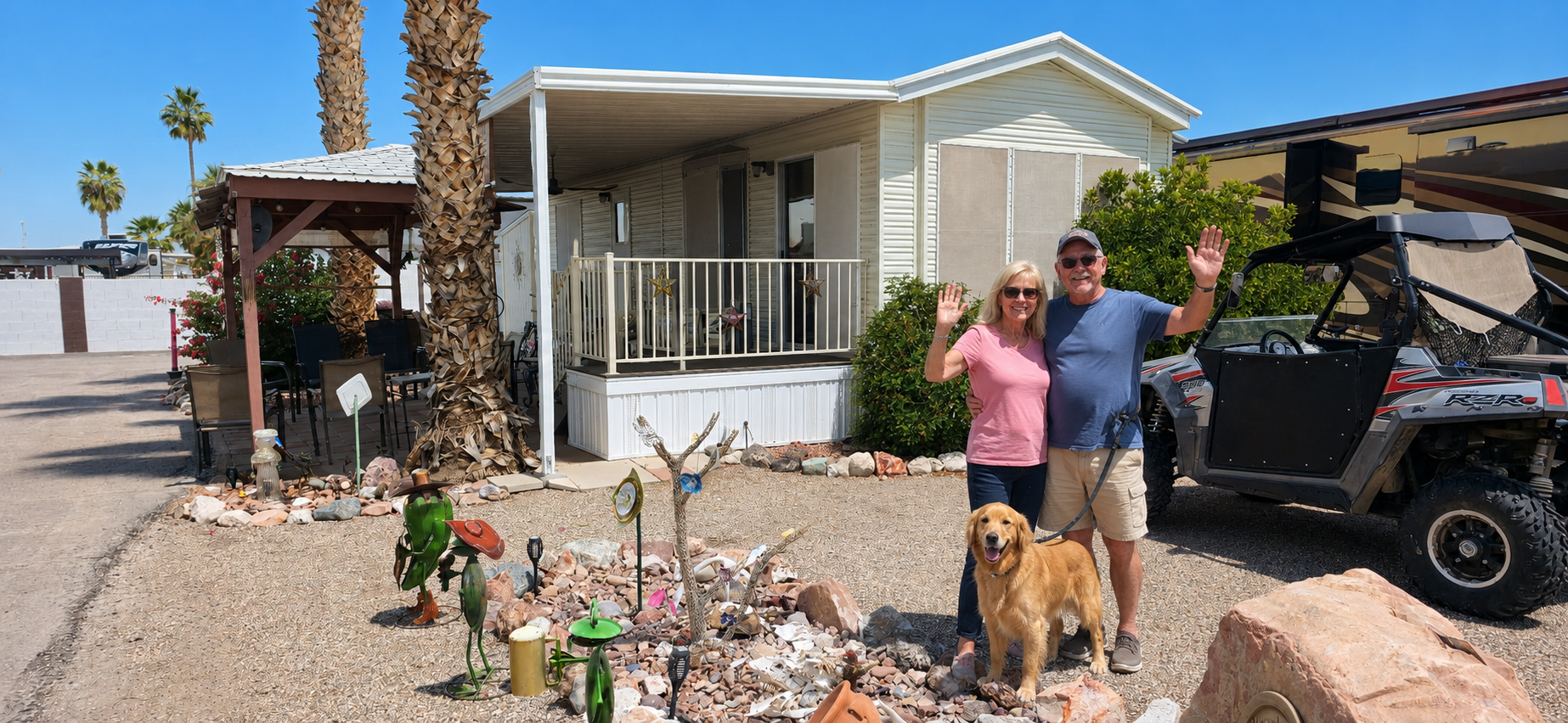 Couple and dog beside a small house in a desert RV park, with a golf cart parked nearby.