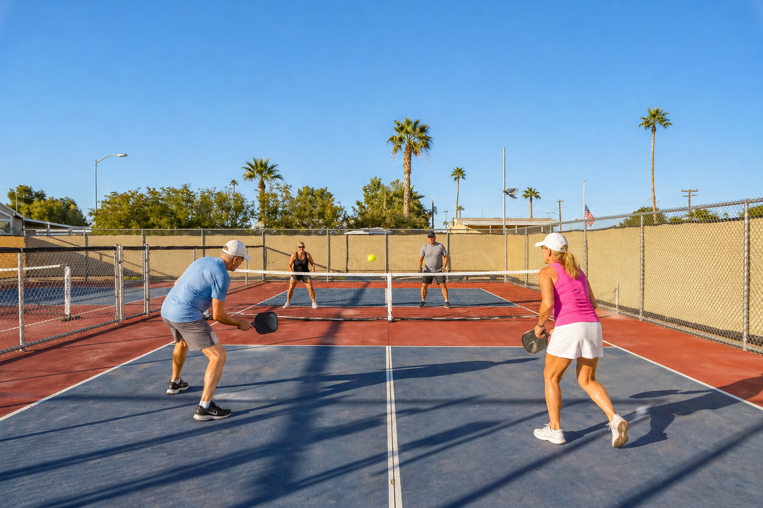 People playing pickleball on an outdoor court, with paddles and a net under a sunny sky.