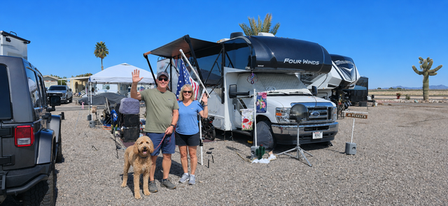 People and a dog camping beside RVs in a desert campsite under a canopy.