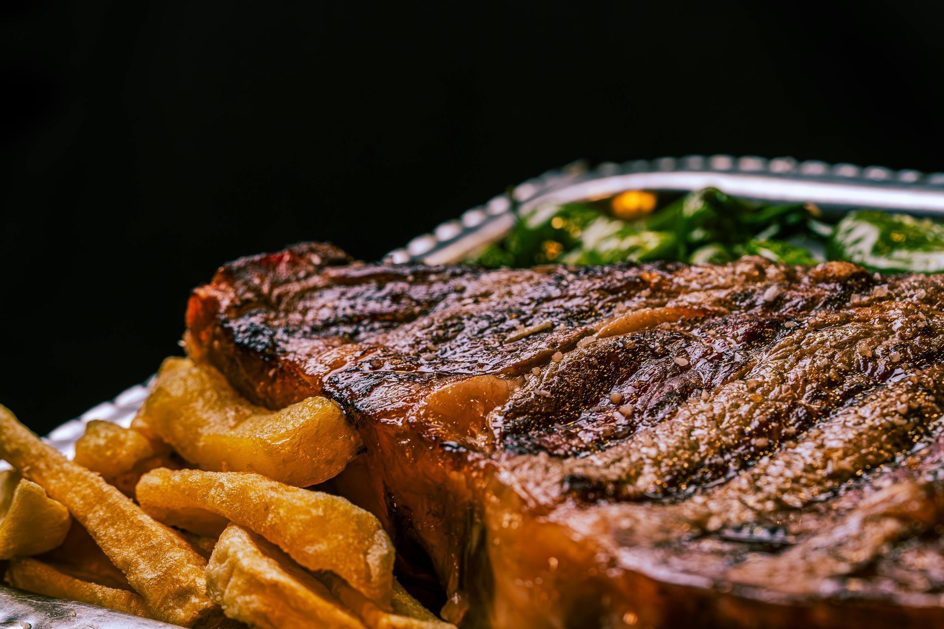 Grilled steak with fries on a black plate, close-up with crisp browned crust