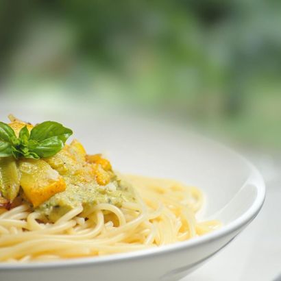Eine Nahaufnahme einer Schüssel Spaghetti mit Soße und Basilikum auf einem Tisch.