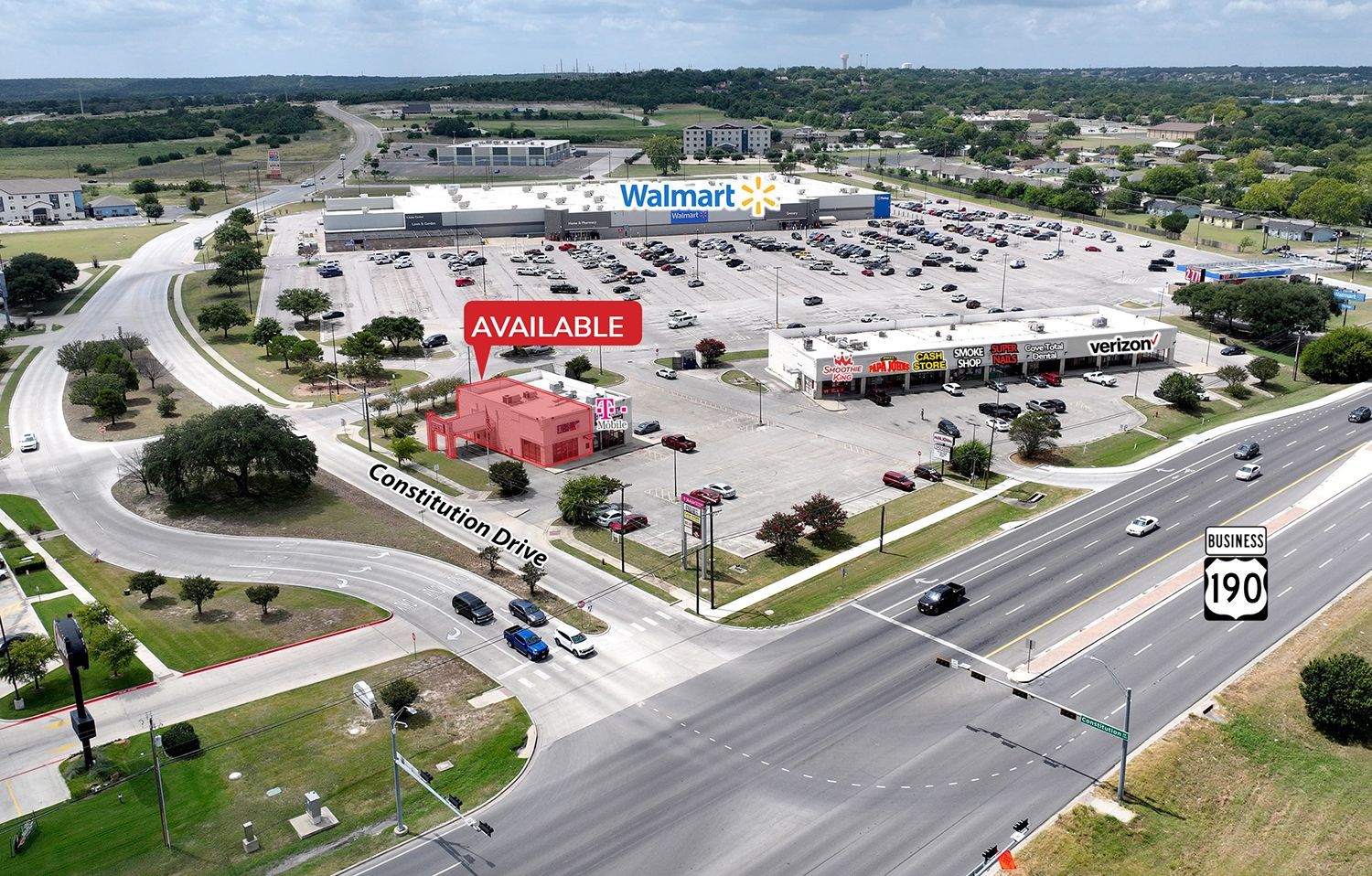 Aerial view of a shopping plaza with multiple stores, parking lots, and a busy intersection on a cloudy day