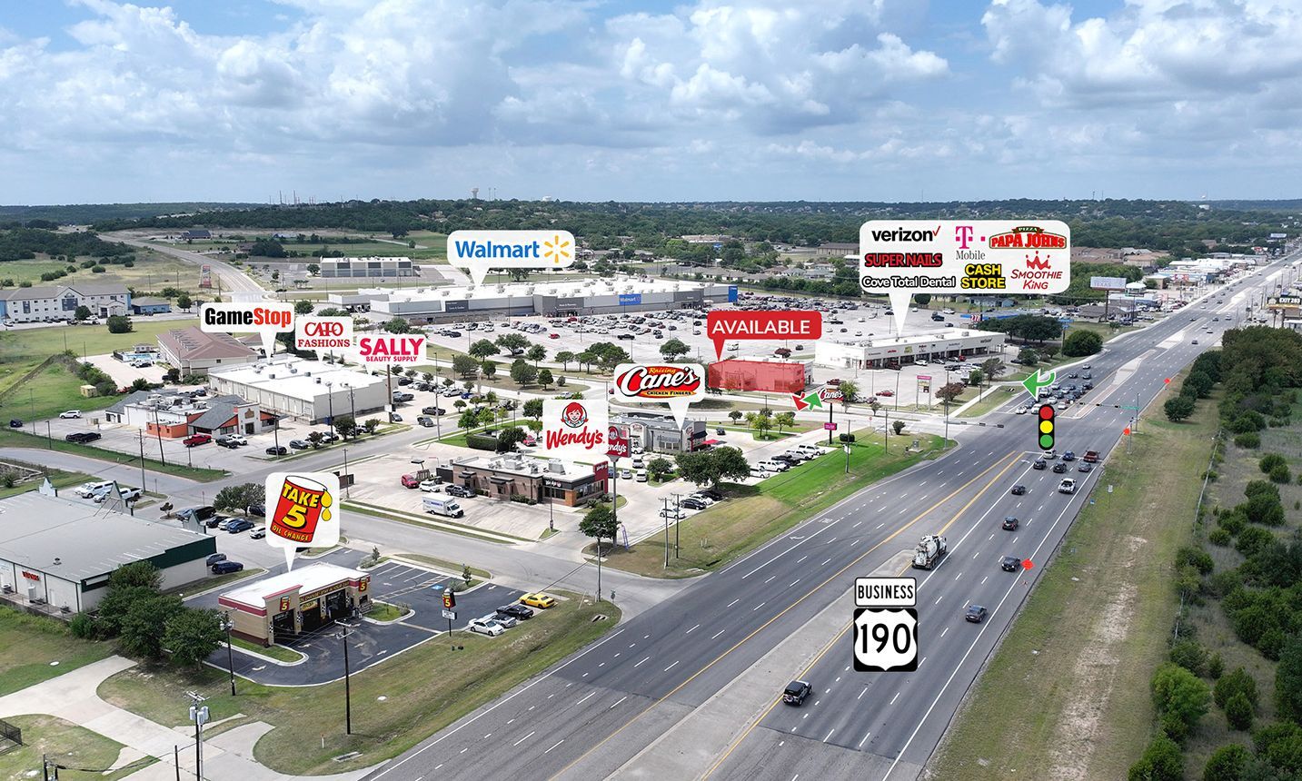 Aerial view of a shopping center and busy highway with store signs and parked cars