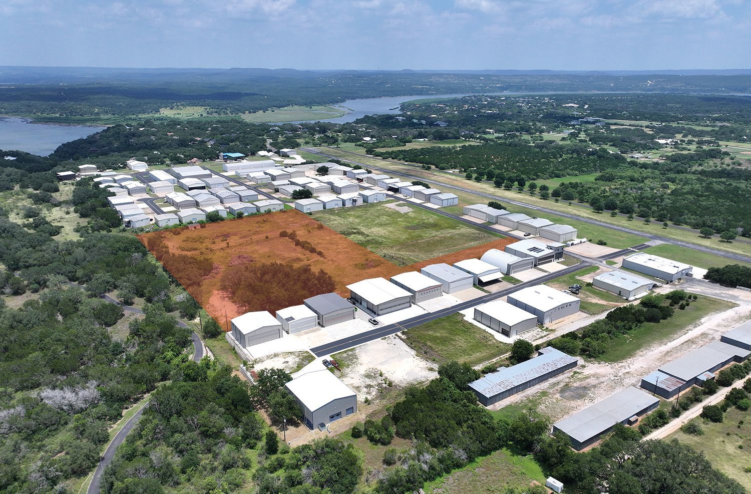 Aerial view of a rural housing development with rows of white-roofed buildings and orange cleared land