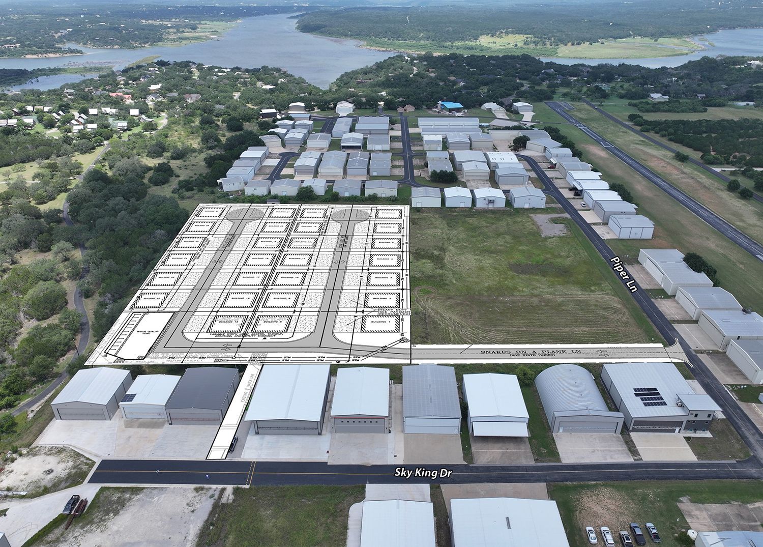 Aerial view of a large industrial warehouse complex beside roads and a river, with trees in the background